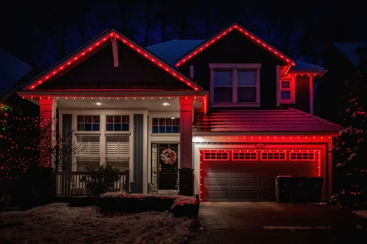 Red permanent lights outlining the roofline and garage of a two-story house at night